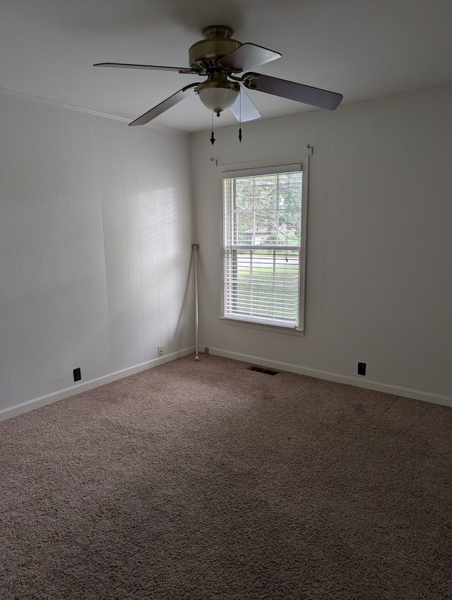 carpeted spare room with wooden walls and ceiling fan