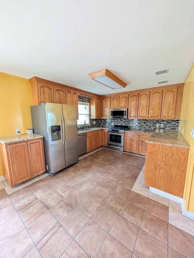 kitchen with appliances with stainless steel finishes, decorative backsplash, light stone counters, light tile patterned floors, and sink