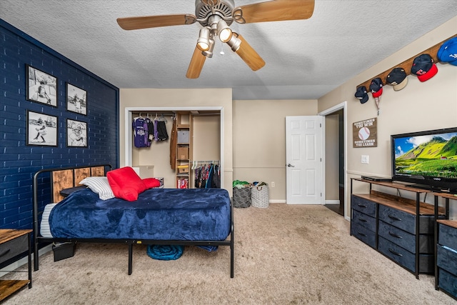 carpeted bedroom featuring a closet, a textured ceiling, a multi sided fireplace, ceiling fan, and brick wall