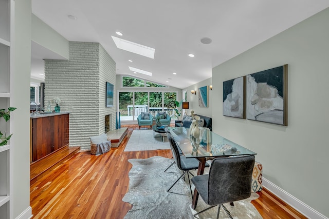 dining area featuring a brick fireplace, wood-type flooring, and vaulted ceiling with skylight