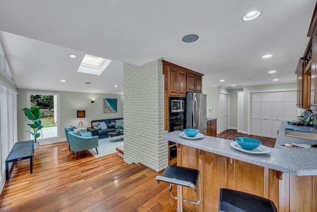 kitchen with a kitchen breakfast bar, stainless steel appliances, kitchen peninsula, and light wood-type flooring