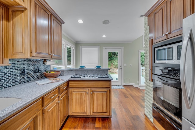 kitchen featuring ornamental molding, appliances with stainless steel finishes, light stone countertops, light hardwood / wood-style floors, and decorative backsplash