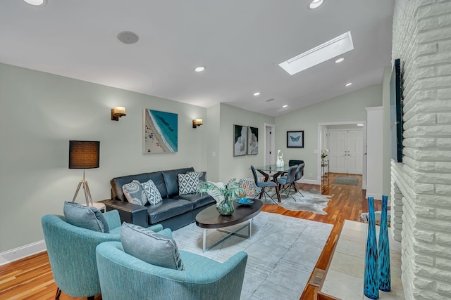 living room featuring hardwood / wood-style floors, lofted ceiling with skylight, and a stone fireplace