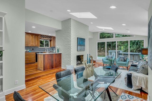 dining space featuring light wood-type flooring, lofted ceiling with skylight, a fireplace, and sink