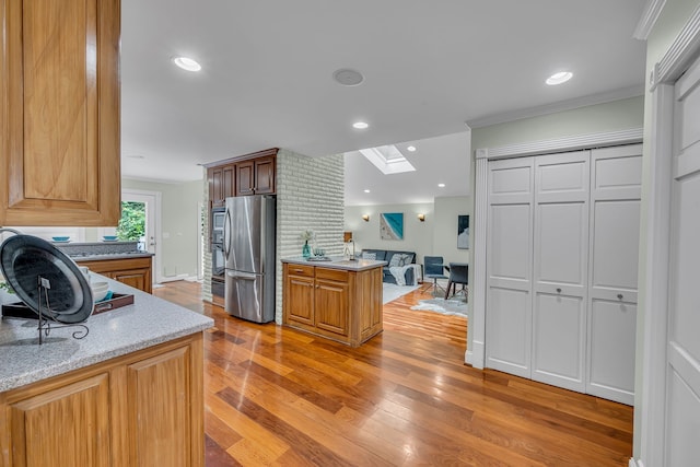 kitchen featuring light stone counters, stainless steel refrigerator, light hardwood / wood-style flooring, a skylight, and ornamental molding