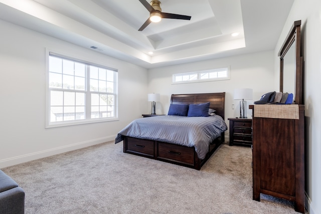 carpeted bedroom featuring multiple windows, a tray ceiling, and ceiling fan