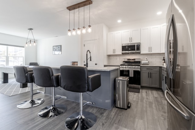 kitchen with appliances with stainless steel finishes, a kitchen breakfast bar, an island with sink, white cabinets, and decorative light fixtures