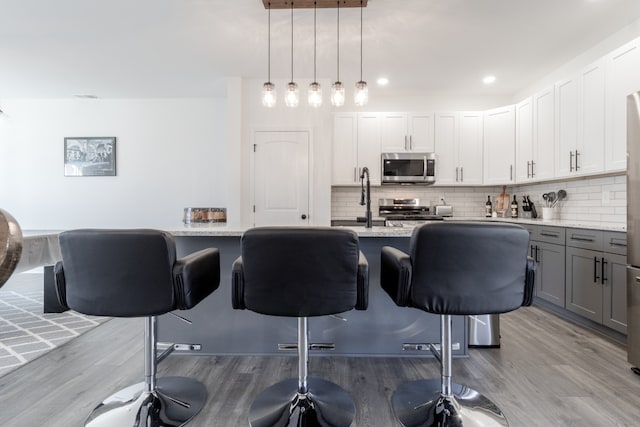 kitchen with white cabinetry, stainless steel appliances, a kitchen bar, and hanging light fixtures