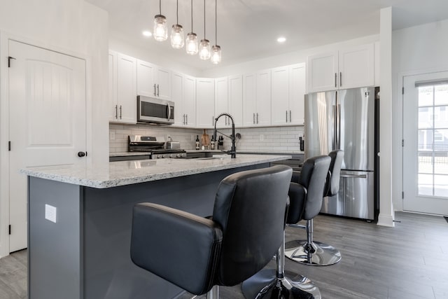 kitchen with pendant lighting, a breakfast bar area, appliances with stainless steel finishes, white cabinets, and a center island with sink