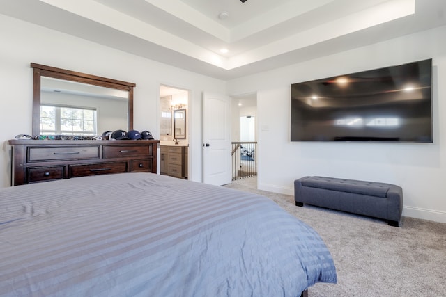 bedroom featuring a raised ceiling, ensuite bathroom, and light colored carpet