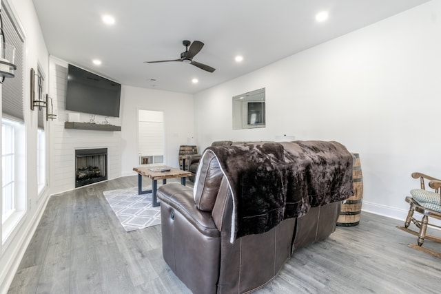 living room with ceiling fan, a large fireplace, and light wood-type flooring