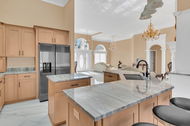 kitchen with light brown cabinetry, sink, a center island, hanging light fixtures, and stainless steel fridge