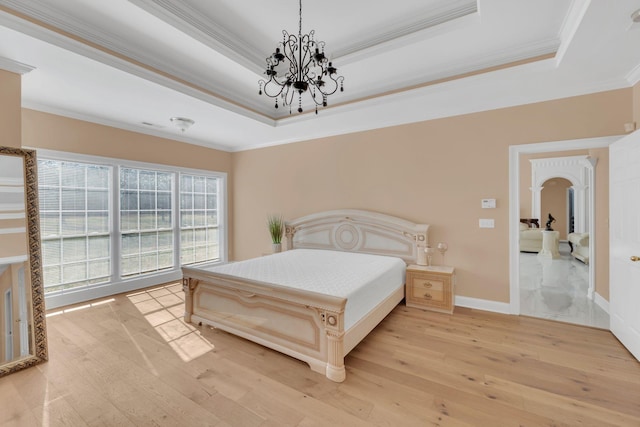 bedroom featuring an inviting chandelier, ornamental molding, a tray ceiling, and light hardwood / wood-style floors