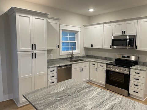 kitchen with light stone counters, appliances with stainless steel finishes, sink, and white cabinetry