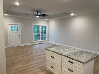 unfurnished living room with light wood-type flooring, a tray ceiling, and ceiling fan