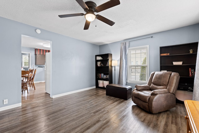 living area featuring ceiling fan, dark wood-type flooring, and a textured ceiling