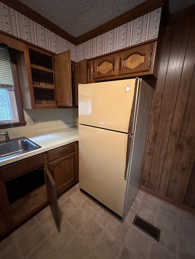 kitchen with a textured ceiling, sink, white fridge, wooden walls, and ornamental molding