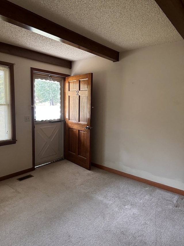 interior space featuring light colored carpet, beamed ceiling, and a textured ceiling