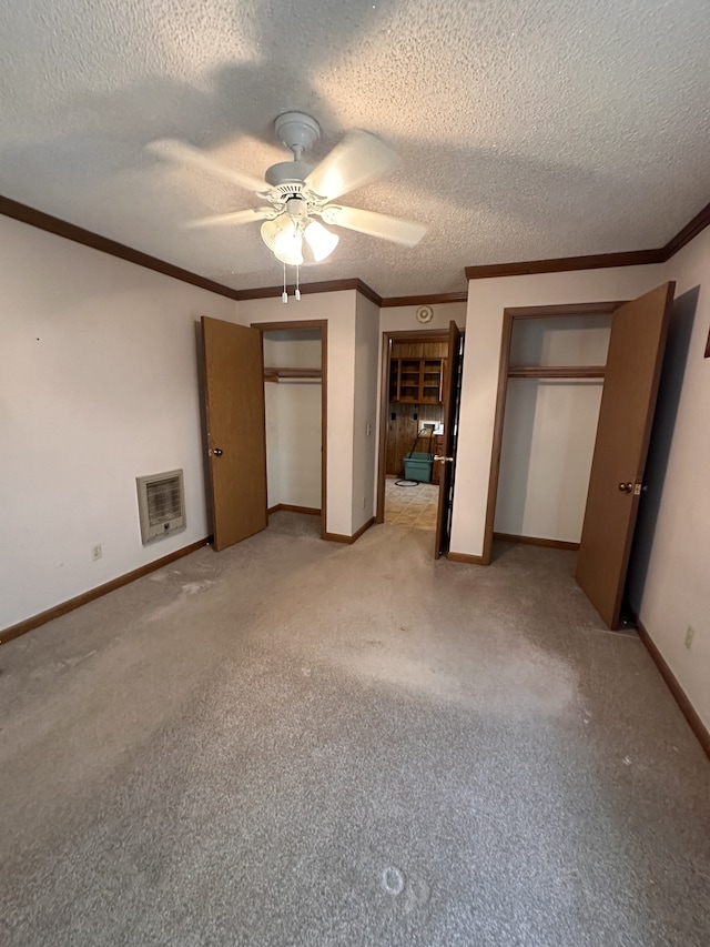 unfurnished bedroom with heating unit, a textured ceiling, light carpet, two closets, and ceiling fan