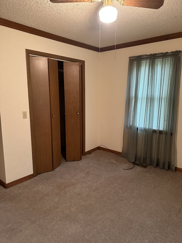 unfurnished bedroom featuring a closet, a textured ceiling, light colored carpet, and crown molding