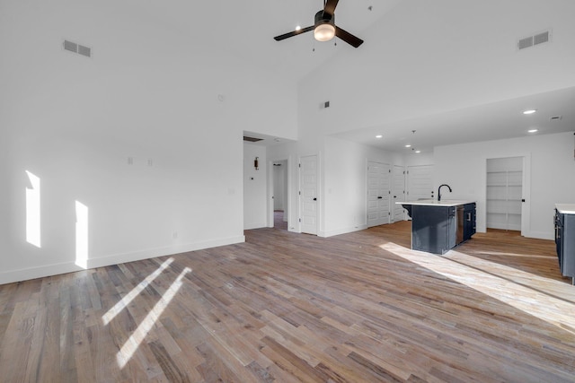 unfurnished living room featuring a high ceiling, sink, light hardwood / wood-style flooring, ceiling fan, and built in features