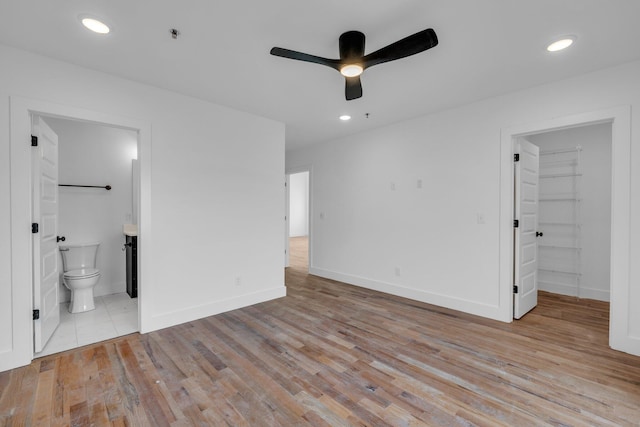 unfurnished bedroom featuring a walk in closet, ensuite bath, ceiling fan, light hardwood / wood-style floors, and a closet