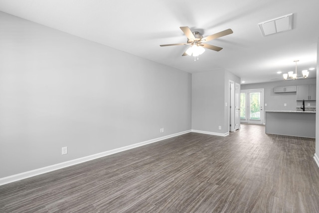 unfurnished living room with dark wood finished floors, baseboards, visible vents, and ceiling fan with notable chandelier