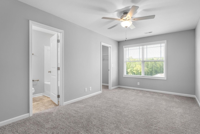 unfurnished bedroom with a walk in closet, carpet floors, visible vents, and baseboards