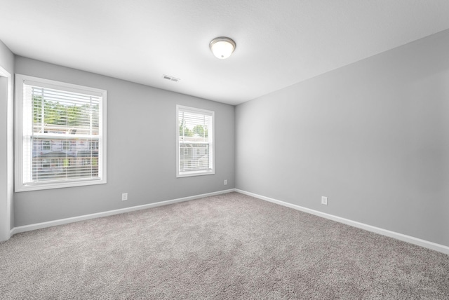 carpeted empty room featuring a healthy amount of sunlight, baseboards, and visible vents