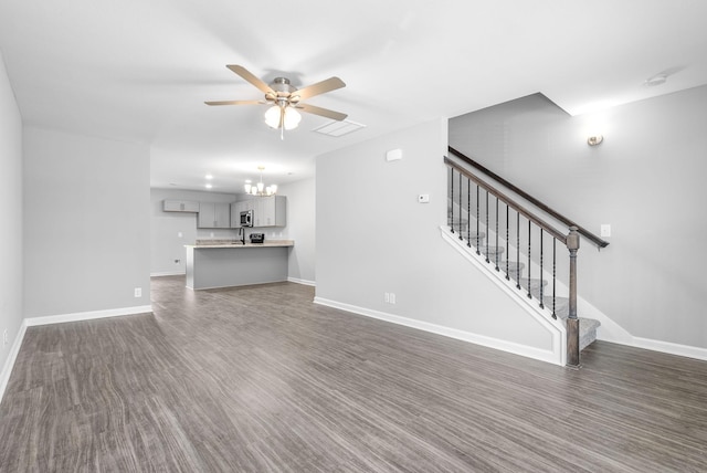 unfurnished living room featuring stairs, baseboards, and ceiling fan with notable chandelier