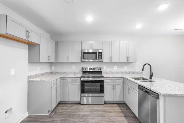 kitchen with stainless steel appliances, a peninsula, a sink, light wood-style floors, and light stone counters