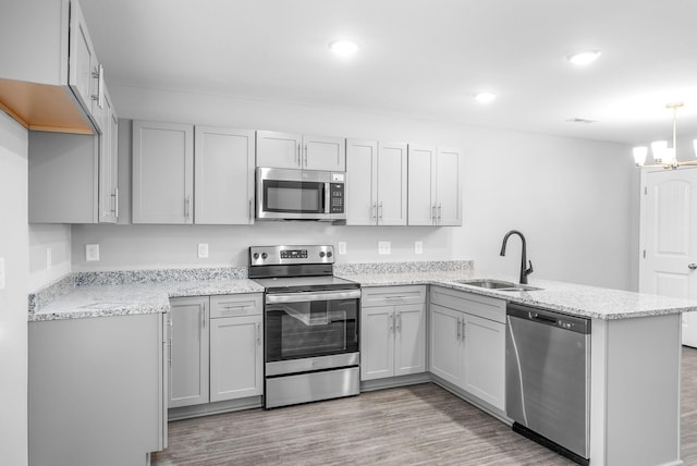 kitchen featuring a peninsula, appliances with stainless steel finishes, light stone countertops, and a sink