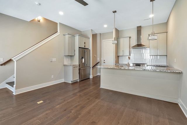 kitchen with light stone counters, pendant lighting, high quality fridge, wall chimney exhaust hood, and dark hardwood / wood-style flooring