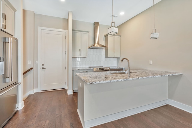 kitchen featuring light stone counters, wall chimney exhaust hood, stainless steel appliances, decorative light fixtures, and dark hardwood / wood-style flooring