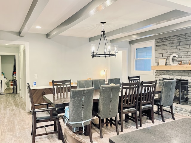 dining room featuring beam ceiling, a stone fireplace, light hardwood / wood-style flooring, and an inviting chandelier