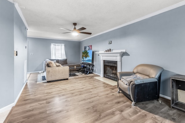 living room with ceiling fan, a high end fireplace, a textured ceiling, light wood-type flooring, and crown molding