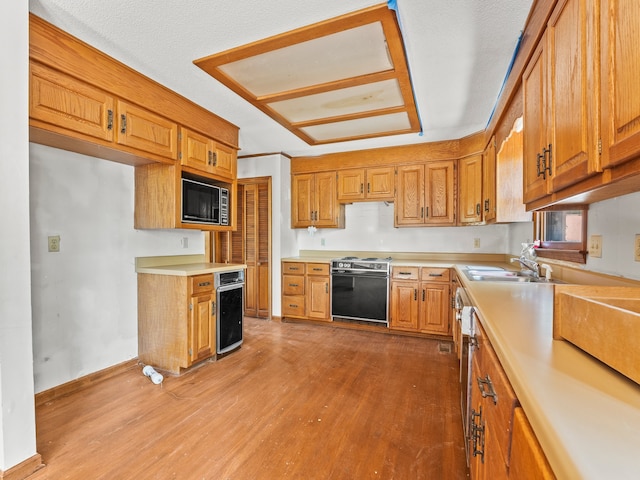 kitchen with electric range oven, light wood-type flooring, a textured ceiling, built in microwave, and sink