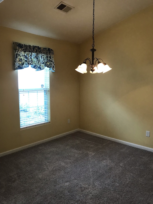 empty room featuring dark colored carpet and a chandelier