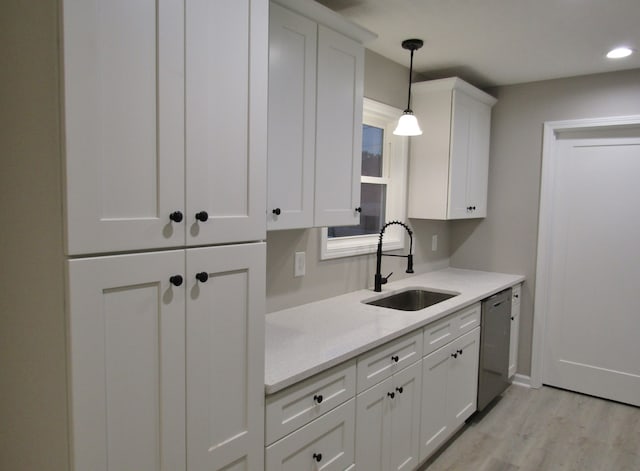 kitchen with hanging light fixtures, white cabinets, light wood-type flooring, stainless steel dishwasher, and sink