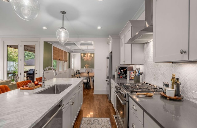 kitchen with wall chimney exhaust hood, premium appliances, decorative light fixtures, dark hardwood / wood-style floors, and sink