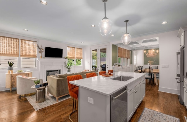 kitchen with hanging light fixtures, sink, a kitchen island with sink, white cabinetry, and dark hardwood / wood-style flooring