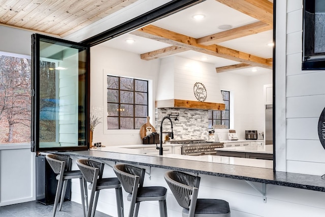 kitchen with beamed ceiling, custom exhaust hood, decorative backsplash, and a kitchen bar