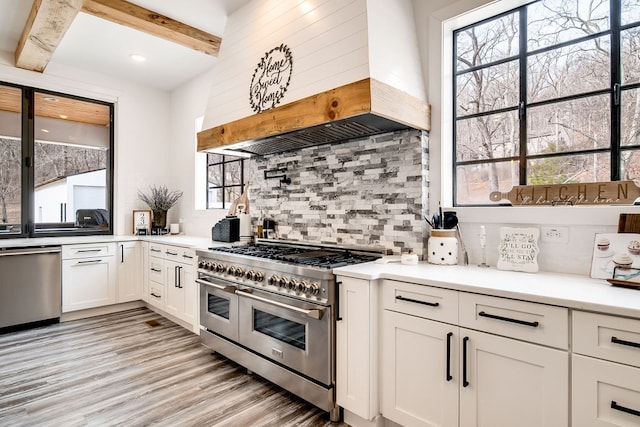 kitchen with appliances with stainless steel finishes, backsplash, white cabinetry, beamed ceiling, and custom exhaust hood