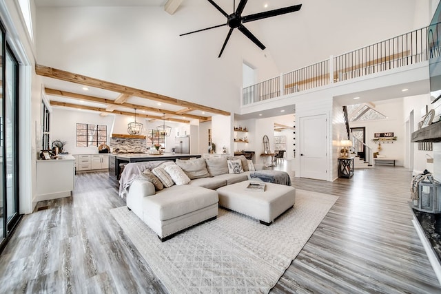 living room featuring ceiling fan, high vaulted ceiling, beamed ceiling, and light hardwood / wood-style flooring