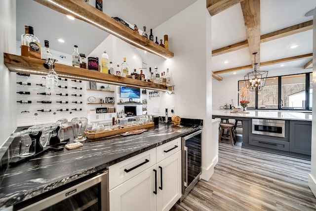 bar featuring white cabinetry, dark stone countertops, beverage cooler, and light wood-type flooring