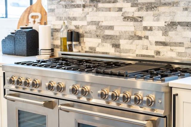 interior details featuring white cabinetry, high end stainless steel range, and tasteful backsplash