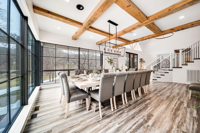 dining space featuring beam ceiling, a chandelier, wood-type flooring, and a towering ceiling