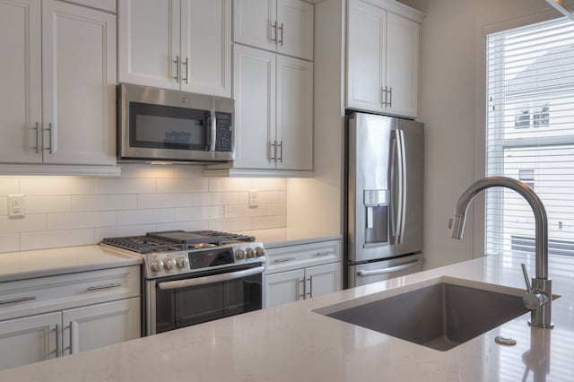 kitchen with white cabinetry, light stone counters, backsplash, stainless steel appliances, and sink