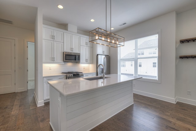 kitchen with dark hardwood / wood-style floors, sink, hanging light fixtures, stainless steel appliances, and a center island with sink