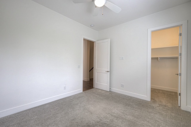 unfurnished bedroom featuring a spacious closet, a closet, carpet, and ceiling fan